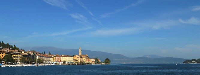 Anti Stress beliebte Urlaubsziele am Gardasee -  Mit einer Fläche von 370 km² ist der Gardasee der größte See Italiens. Es liegt am Fuße der Alpen und erstreckt sich über drei Staaten: Lombardei, Venetien und Trentino. Die maximale Tiefe des Sees beträgt 346 m, er hat eine längliche Form und sein nördliches Ende ist sehr schmal. Dort ist der See von den Bergen der Gruppo di Baldo umgeben. Du trittst aus deinem gemütlichen Hotelzimmer und es begrüßt dich die warme italienische Sonne. Du blickst auf den atemberaubenden Gardasee, der in zahlreichen Blautönen schimmert - von tiefem Dunkelblau bis zu funkelndem Türkis. Majestätische Berge umgeben dich, während die Brise sanft deine Haut streichelt und der Duft von blühenden Zitronenbäumen deine Nase kitzelt. Du schlenderst die malerischen, engen Gassen entlang, vorbei an farbenfrohen, blumengeschmückten Häusern. Vereinzelt unterbricht das fröhliche Lachen der Einheimischen die friedvolle Stille. Du fühlst dich wie in einem Traum, der nicht enden will. Jeder Schritt führt dich zu neuen Entdeckungen und Abenteuern. Du probierst die köstliche italienische Küche mit ihren frischen Zutaten und verführerischen Aromen. Die Sonne geht langsam unter und taucht den Himmel in ein leuchtendes Orange-rot - ein spektakulärer Anblick.